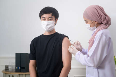 A female muslim doctor injecting covid-19 vaccine to patient arm, covid-19 vaccination and health care conceptの写真素材