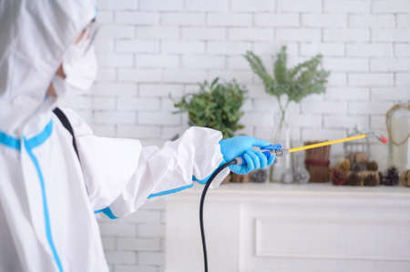 A medical staff in PPE suit is using disinfectant spray in living room, Covid-19 protection , disinfection concept .の写真素材