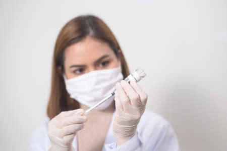 A young female doctor holding a syringe with covid-19 vaccine bottle for injection, covid-19 vaccination and health care conceptの写真素材