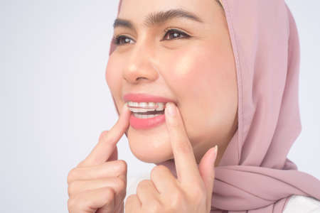 A young muslim woman holding colorful retainer for teeth over white background studio, dental healthcare and Orthodontic concept.の写真素材