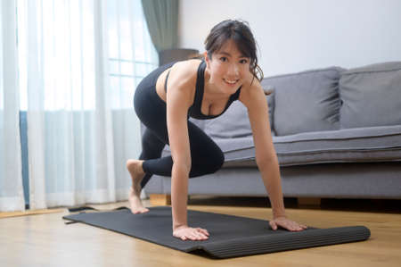 A happy young woman in sportswear is exercising in living room at homeの写真素材