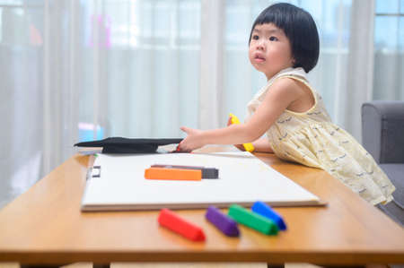Baby girl drawing with colored pencils in living room at home.
