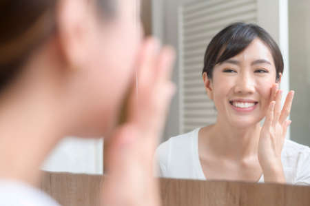 A happy beautiful woman applying moisturizing cream on face, skin care and treatment conceptの写真素材
