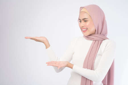 A portrait of young smiling muslim woman wearing a pink hijab over white background studio.の写真素材