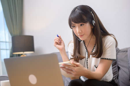 A beautiful young woman wearing headset is making video conference call via computer at home