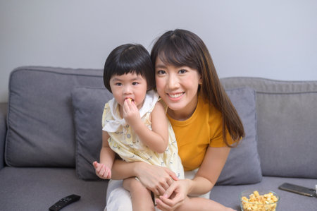 A happy mom and daughter watching movie and relaxing at homeの写真素材