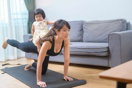 A happy young woman in sportswear is with daughter exercising in living room at homeの写真素材