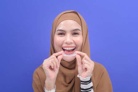 A young muslim woman holding invisalign braces in studio, dental healthcare and Orthodontic concept.