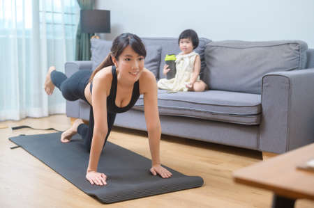 A happy young woman in sportswear is with daughter exercising in living room at homeの写真素材