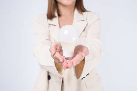 A young businesswoman is holding Light bulb wearing suit over white  background studioの写真素材