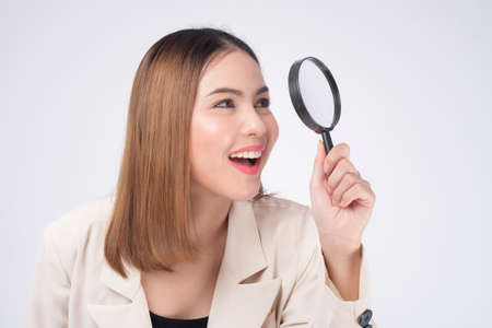 Young beautiful woman in suit holding magnifying glass over white background studioの写真素材