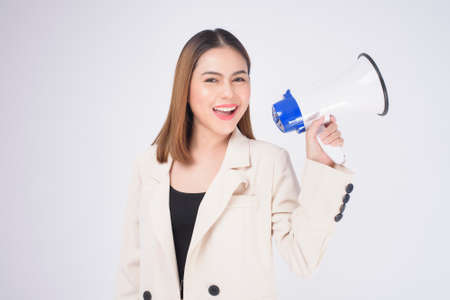 portrait of young beautiful smiling woman in suit using megaphone to announce over isolated white background studioの写真素材