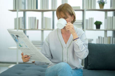 Happy  Caucasian senior woman  is relaxing , reading newspaper in living roomの写真素材