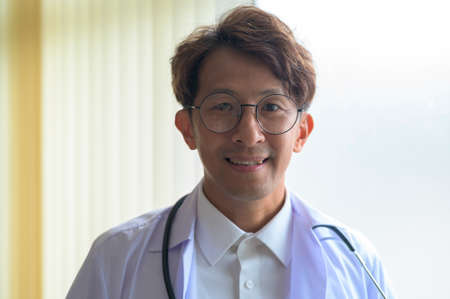 Portrait of confident smiling doctor wearing white coat in hospitalの写真素材