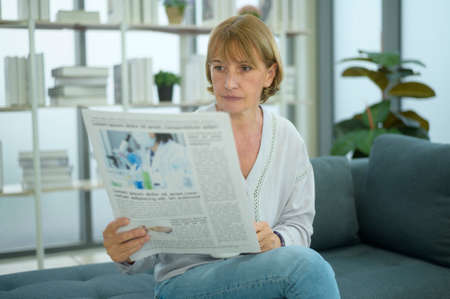 Happy  Caucasian senior woman  is relaxing , reading newspaper in living room