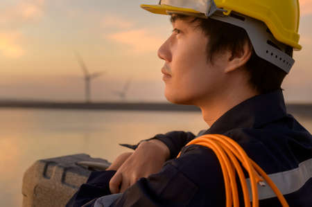 A male engineer wearing a protective helmet at sunset.
