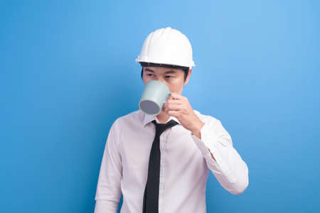 A portrait of confident male engineer wearing a white helmet having a cup of coffee over purple background studioの写真素材