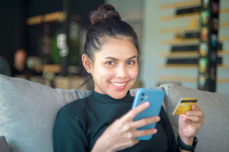 A happy young woman is shopping online via smart phone , holding credit card