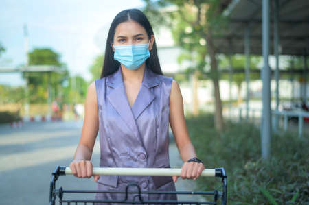 young woman wearing a surgical mask waiting in line near cashier counter in supermarket, covid-19 and pandemic conceptの写真素材