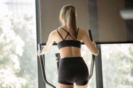 A beautiful woman using an elliptic trainer at gym, concept of healthy lifestyle, sports, training,...