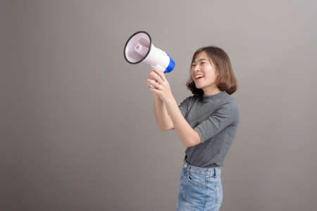 A portrait of young beautiful asian woman holding megaphone over studio background.の写真素材