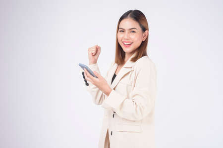 Portrait of young beautiful woman in suit using smart phone over white backgroundの写真素材
