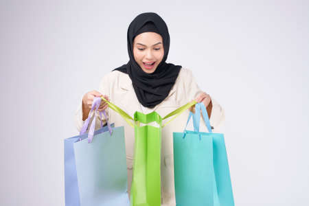 Young beautiful muslim woman in suit holding colorful shopping bags over white background studioの写真素材