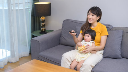 A happy mom and daughter watching movie and relaxing at homeの写真素材