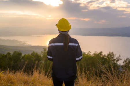 a woman engineer is putting a protective helmet on her head at sunset.の写真素材
