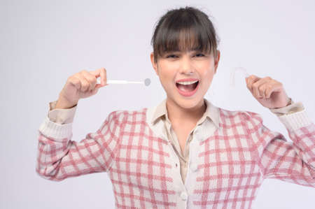 A young smiling woman holding invisalign braces over white background studio, dental healthcare and Orthodontic concept.の写真素材
