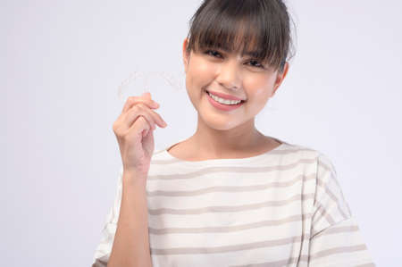 A young smiling woman holding invisalign braces over white background studio, dental healthcare and Orthodontic concept.の写真素材