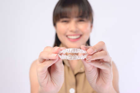 A young smiling woman holding invisalign braces over white background studio, dental healthcare and Orthodontic concept.の写真素材