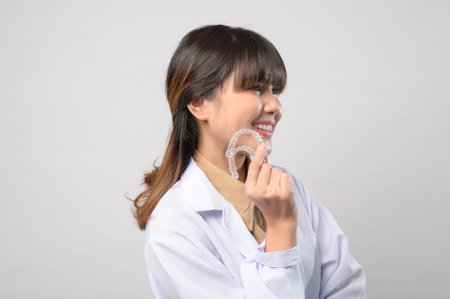A young female dentist holding invisalign braces over white background studio, dental healthcare and...