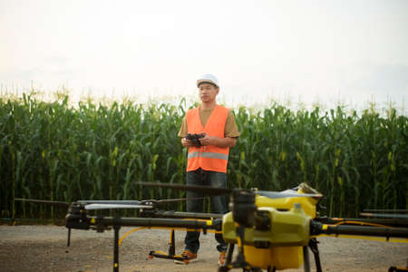 A male engineer controlling drone spraying fertilizer and pesticide over farmland,High technology innovations and smart farmingの写真素材