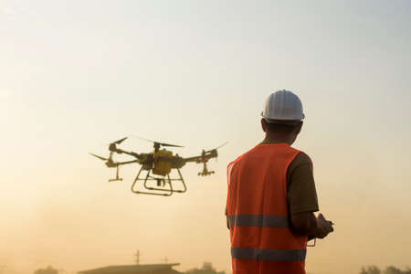 A male engineer controlling drone spraying fertilizer and pesticide over farmland,High technology...