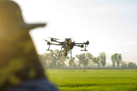 A young smart farmer controlling drone spraying fertilizer and pesticide over farmland,High...