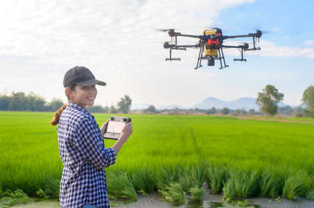 A young smart farmer controlling drone spraying fertilizer and pesticide over farmland,High...