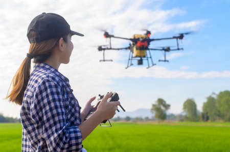 A young smart farmer controlling drone spraying fertilizer and pesticide over farmland,High...