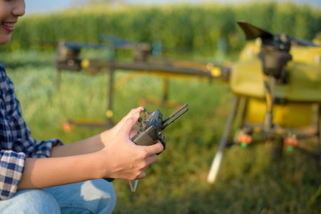 A young smart farmer controlling drone spraying fertilizer and pesticide over farmland,High...