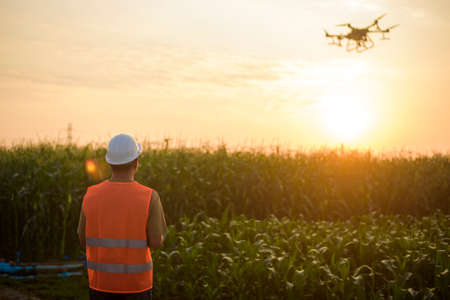 A male engineer controlling drone spraying fertilizer and pesticide over farmland,High technology innovations and smart farmingの写真素材