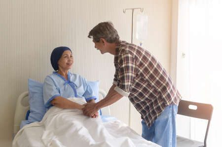 A Senior man visiting cancer patient woman wearing head scarf at hospital, health care and medical...