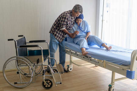 A Senior man helping cancer patient woman wearing head scarf moving to wheelchairs at hospital, health care and medical conceptの写真素材