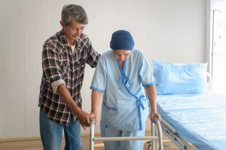 A Senior man helping cancer patient woman wearing head scarf with walker at hospital, health care and medical conceptの写真素材