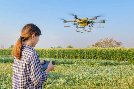 A young smart farmer controlling drone spraying fertilizer and pesticide over farmland,High...