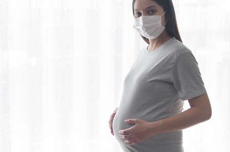 Young pregnant woman wearing a protective mask and expecting a baby, healthy and motherhood conceptの写真素材