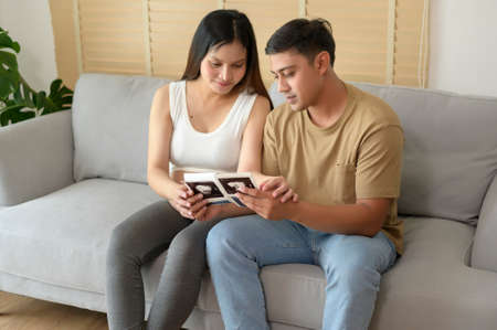 Young pregnant woman with husband holding ultrasound photo of newborn baby, maternity and family conceptの写真素材