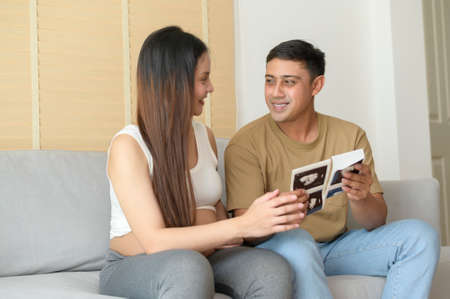 Young pregnant woman with husband holding ultrasound photo of newborn baby, maternity and family conceptの写真素材
