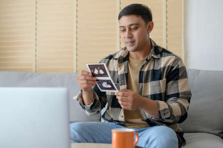 Young father holding ultrasound photo of newborn baby, maternity and family conceptの写真素材