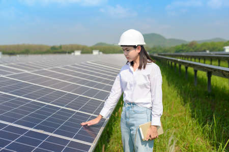 A female engineer wearing helmet in Photovoltaic Cell Farm or Solar Panels Field, eco friendly and...