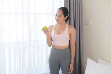 Fit young woman eating an apple after work out at home, sport and healthy lifestyle concept.